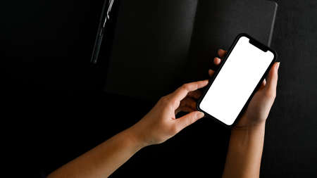 Top view, flat lay, Female hands using modern mobile phone on modern black worktable. female holding smartphone blank screen mockup.の写真素材