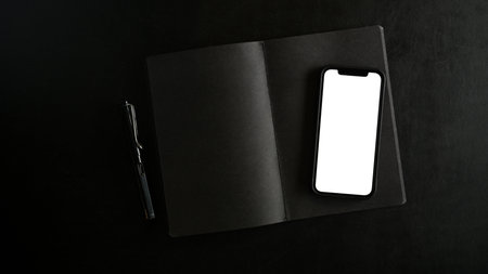 Modern smartphone in white blank screen mockup on an opened notebook on black background. top view,...