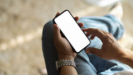 Close-up, top view of a man relaxed at his living room and using a modern smartphone. mobile phone white screen mockup.の写真素材