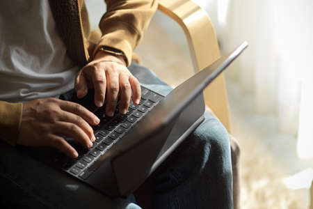 Cropped image of a hipster man sits on a chair and working, typing on portable tablet keyboard at his house.の写真素材