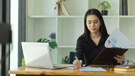 Asian young financial woman working with laptop computer and financial report at her office desk.の写真素材