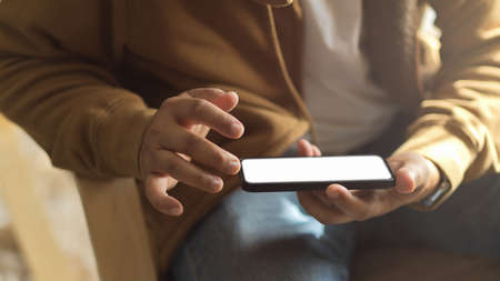 Cropped shot a man sitting on arm chair and watching video on mobile phone. smartphone blank screen mockup.の写真素材