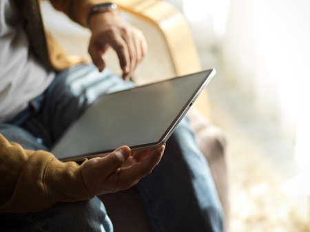 An adult man sitting at his arm chair and using modern digital tablet computer. relaxed man with digital technology concept.の写真素材
