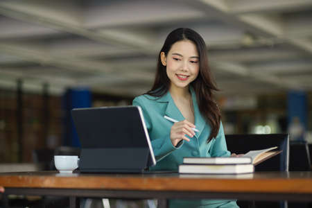 Attractive young female working on tablet computer and researching an informations on a books at library.の写真素材