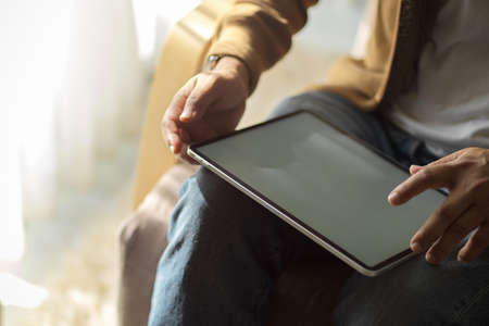 Cropped image of a man sitting on a sofa and using digital tablet computer at his living room.の写真素材
