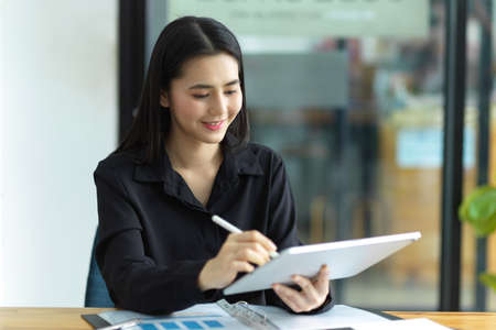 Cheerful business woman working on her portable graphic tablet computer at her studio office.の写真素材