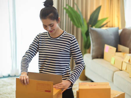 Beautiful female online store owner, small business entrepreneur packing package for ready to ship to her customer. post parcel boxes. e-commerce.の写真素材