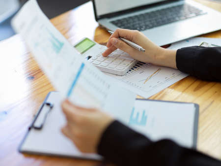 Cropped image of Female accountant calculating company financial expense with report and calculator in office.の写真素材