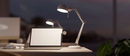 Modern dark office studio interior with laptop computer white screen mockup under table lamp....