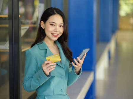 A stunning business woman holding credit card and smart mobile phone. internet banking, online payment, money transfer concept.の写真素材
