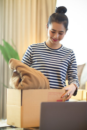 Portrait of young female small business owner packing clothes in a parcel box. e-commerce business...