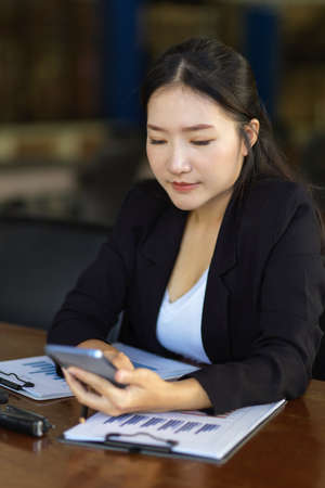 Portrait of an adult female manager in formal suit sitting at her desk and using mobile phone. online communication concept.の写真素材