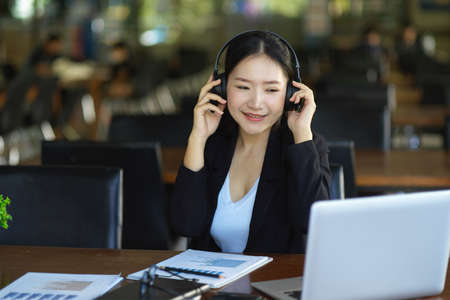 A businesswoman put on headphones to make a video call with a client. Business and remote work concept.の写真素材