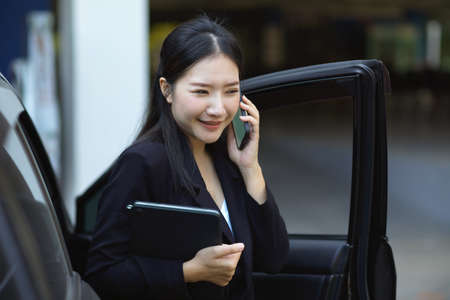 A confident executive female manager speaks on the phone while getting out of her car. businesswoman concept.の写真素材