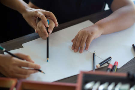 An adult woman assists and instructs her younger sister in using color pencils to draw and paint on paper. close-upの写真素材