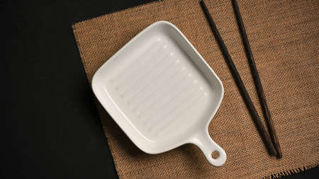 Modern white small pan plate with chopsticks on placemat over black dining table. top viewの写真素材