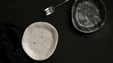 Handmade craft ceramic plates set with fork on black background. ceramic crockery. top viewの写真素材
