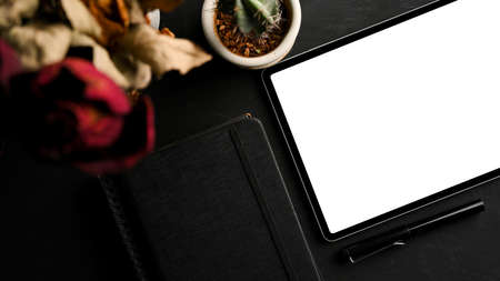 Modern dark working table with digital tablet blank screen mockup, diary book and dry flowers. top viewの写真素材