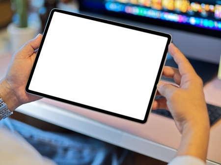 Close-up image of a man's hands holding digital tablet computer with white screen mockup at his deskの写真素材