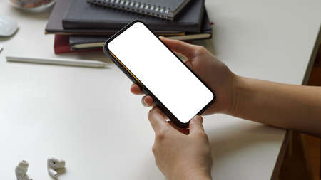 Businesswoman hands holding smart phone with white blank empty screen on simple white desk table.