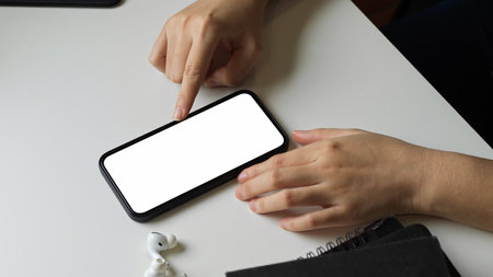 Close-up a female hand using smart phone with white blank empty screen on white desk table.の写真素材
