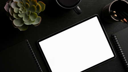 Portable tablet computer with white screen mockup and accessories on modern dark working desk. top viewの写真素材