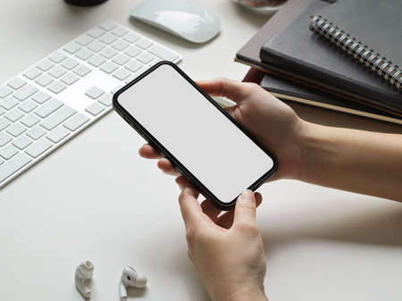 Cropped shot of businesswoman hands using smartphone mockup at the white office desk. phone blank screen mockupの写真素材