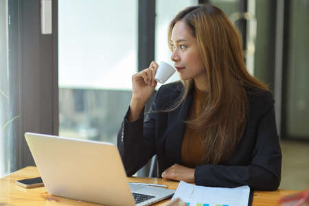 Relaxed business woman sipping her morning coffee at her office workplace. business woman with her coffee break concept.の写真素材