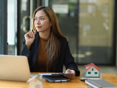 Attractive and beautiful asian young businesswoman dreamed about her success while working at her desk. thoughtful, daydreaming, thinking, pondering.の写真素材