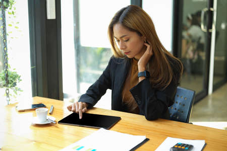 Beautiful Asian businesswoman or working woman working on a digital tablet computer at the office.の写真素材