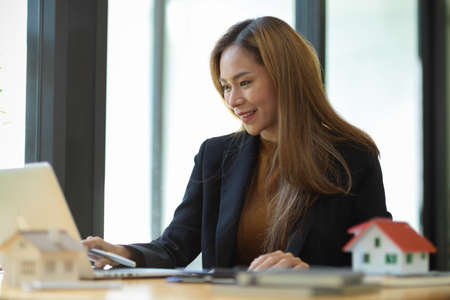 Attractive asian female real estate agent working or checking her rental contract document on laptop computer at the office.の写真素材