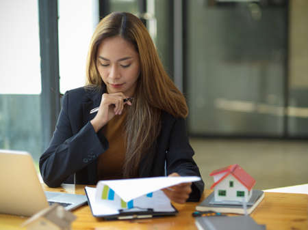 Attractive asian businesswoman or financial consultant focused on her financial report paperwork at the office.の写真素材
