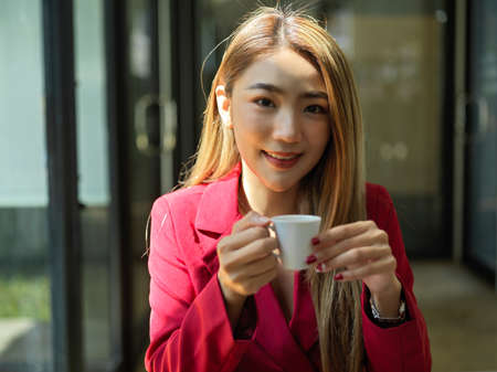 Close-up image of Beautiful asian young business woman holding hot coffee cup, relaxing at workplace.の写真素材