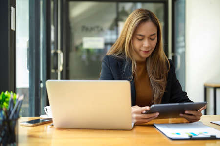 Asian young female assistant or marketing worker working at her desk, using digital tablet computer.の写真素材