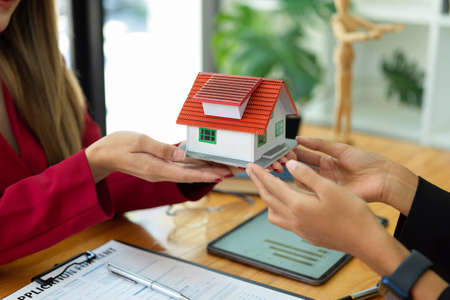 Cropped shot of female real estate agent holding house model at theirs office workplace. property investment, house rental business concept.の写真素材