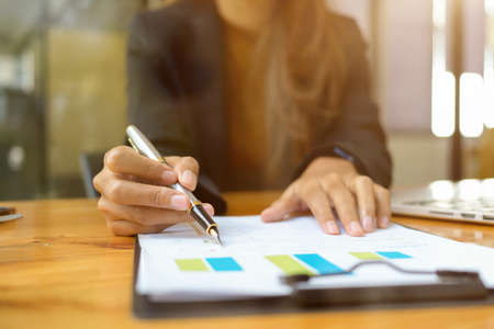 Female financial consultant examines a financial data report paperwork at her office desk. pen pointing on paper.の写真素材