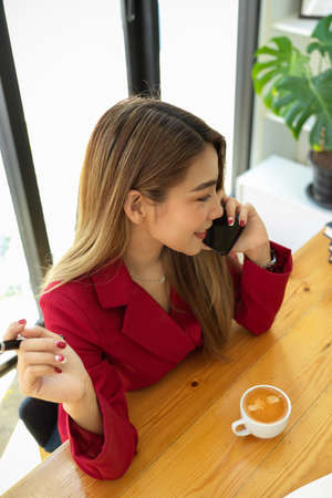 Elegant and confident business woman talking on the phone with her friends, sitting at coffee shop.の写真素材
