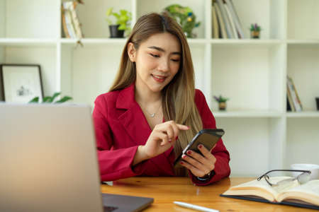 Beautiful young business woman chatting with her friends on mobile application. Female using smartphone at the desk.の写真素材