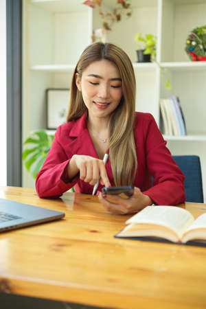 Portrait of asian female manager using her smart mobile phone at her working desk in the office.の写真素材