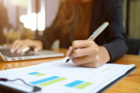 Close-up female's hand writing something on financial report paperwork at the desk. business people concept.の写真素材