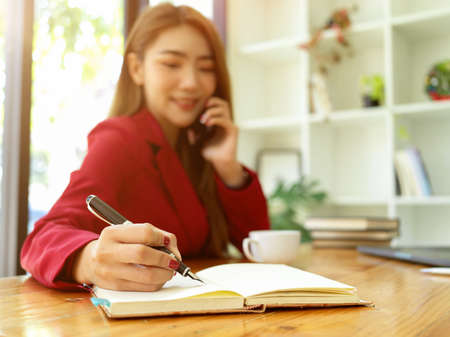An asian female assistant taking a notes while talking on the phone with her boss in the office.の写真素材