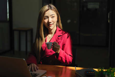 Successful executive female manager sipping a shot of espresso during working on her laptop computerの写真素材