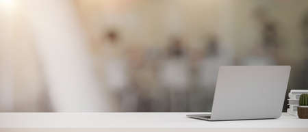 Modern workspace with portable laptop computer and copy space on office desk over blurred office background. 3d rendering, 3d illustrationの写真素材