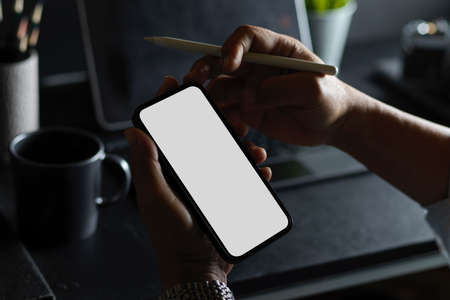 Close-up, A man's hands holding smartphone blank screen mockup on modern dark workplace.の写真素材