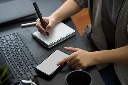 A female taking notes on notepad while looking an informations on smartphone at her office workplaceの写真素材