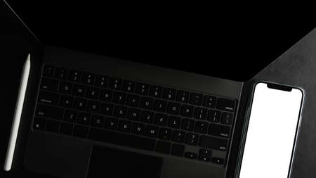 Close-up, top view of a modern black tablet or touchpad computer with smartphone blank screen on a desk.の写真素材