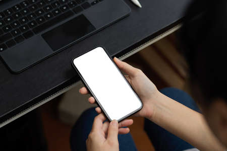Close-up image of a woman holding smartphone on her working desk in the office. blank screen mockup.の写真素材