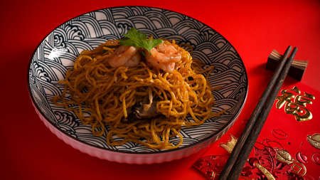 Shrimp chow mein or Chinese stir fried noodle with shrimp on a plate and chopstick on a red background. Translation: Fu meaning good fortuneの写真素材