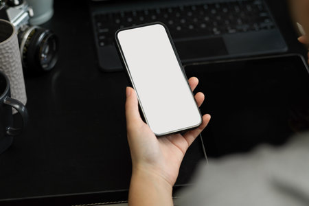 Modern mobile phone blank screen mockup for your graphic display on a female hand at working desk.の写真素材