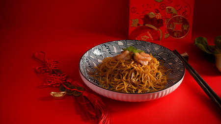 A plate of chow mein with shrimps, chopsticks, Chinese lucky charms, Chinese new year card on a red background.の写真素材